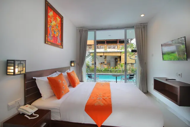A bedroom with a made king bed with orange accents, a wall-mounted television, and sliding glass doors looking out onto a swimming pool.