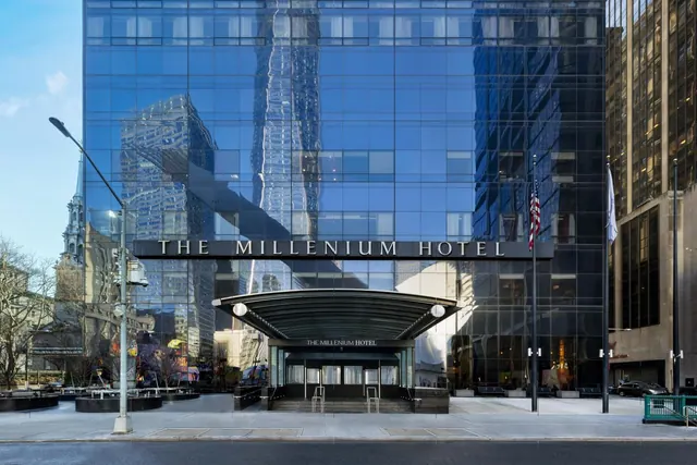 The glass facade of The Millennium Hotel with its entrance canopy, flagpoles and empty street frontage in daylight.