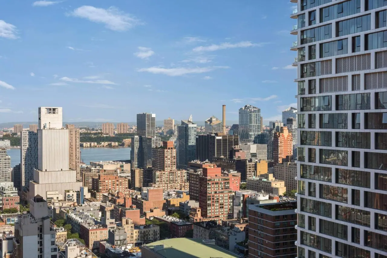 A high-level view over a dense city skyline with a river visible on the left and a tall glass residential tower on the right.