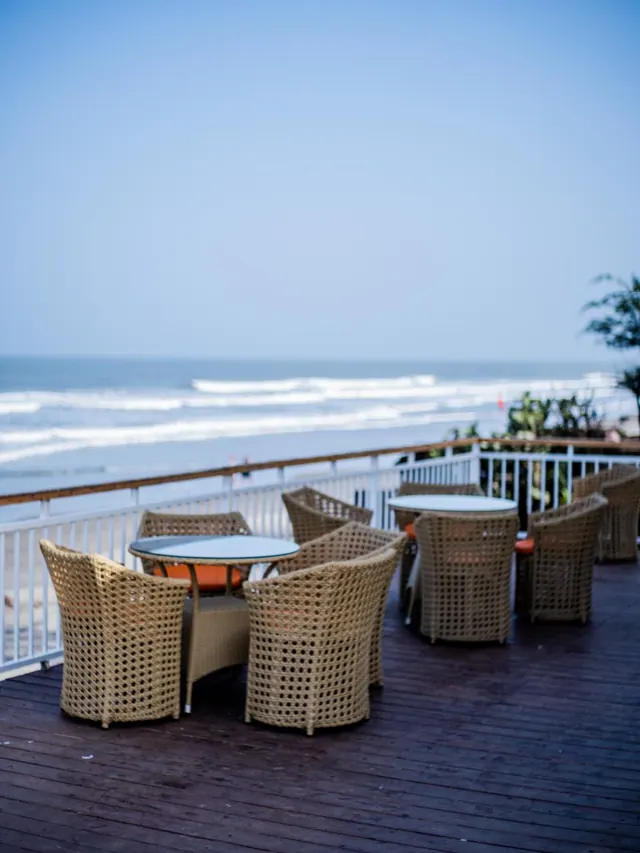 An outdoor terrace with wicker dining furniture overlooks the sea.