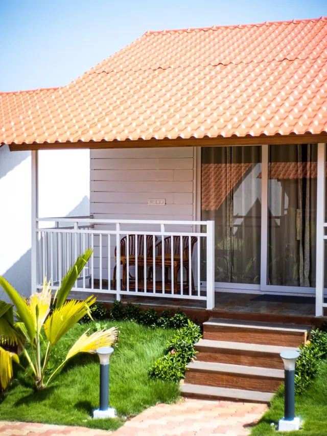 A tiled-roof bungalow has a furnished balcony, glass doors, and steps leading through a landscaped garden.