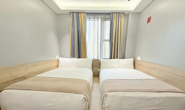 Two made-up beds with wooden headboards sit either side of a room with a window draped in striped curtains.