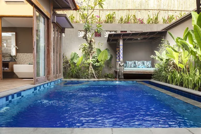 A private swimming pool in a walled courtyard, with a daybed under a wooden pergola, a stone statue fountain, and a freestanding bathtub visible through glass doors on the left.