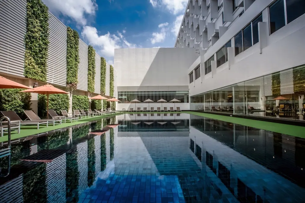 A long outdoor lap pool with dark tiles and sun loungers under orange umbrellas, flanked by vertical green walls and a white hotel building.