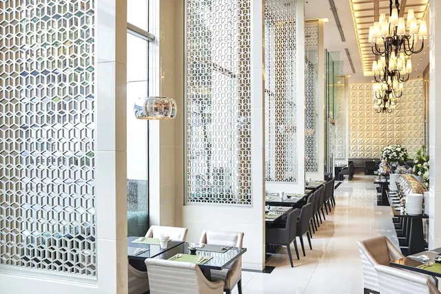 A restaurant dining room with decorative lattice partition screens, set tables and chairs, a chandelier, and a buffet counter along the right side.