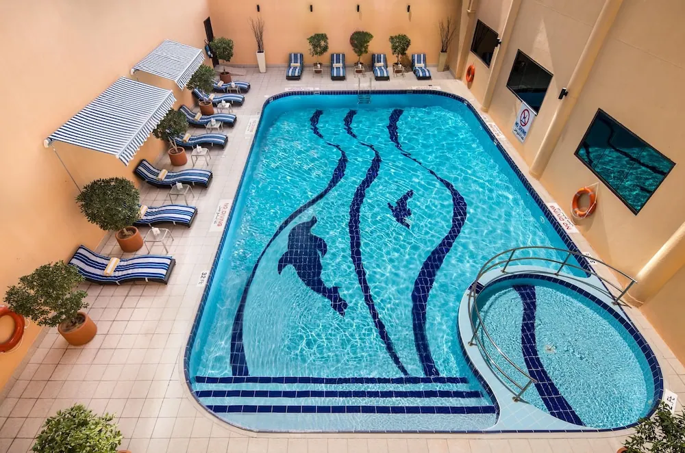Overhead view of an outdoor pool with a dolphin mosaic on its floor, striped loungers along the edge, and a round jacuzzi attached at one end.