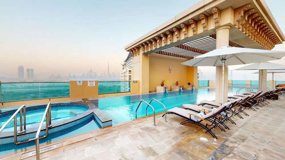 A rooftop pool with an attached hot tub, sun loungers and umbrellas, with a hazy city skyline in the background.