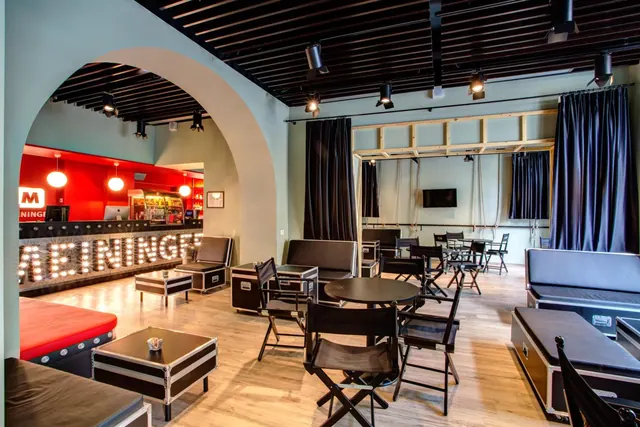 A lounge with a red bar counter, illuminated marquee-style lettering, black director's chairs and flight-case seating on a wooden floor.