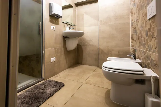 A bathroom with a walk-in glass shower, a wall-hung sink, and a toilet beside a bidet.