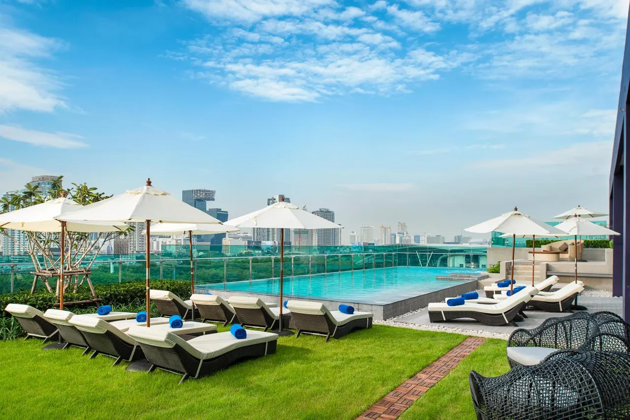 A rooftop swimming pool with white sun loungers and parasols, with a city skyline in the background.