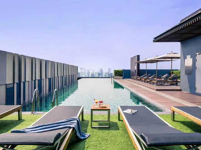 A rooftop lap pool with sun loungers, shade umbrellas and a city skyline visible in the distance.