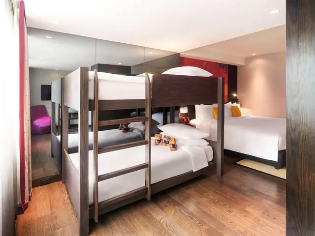A bedroom with a wooden bunk bed and a large double bed, with mirrored wall panels and teddy bears on the lower bunk.