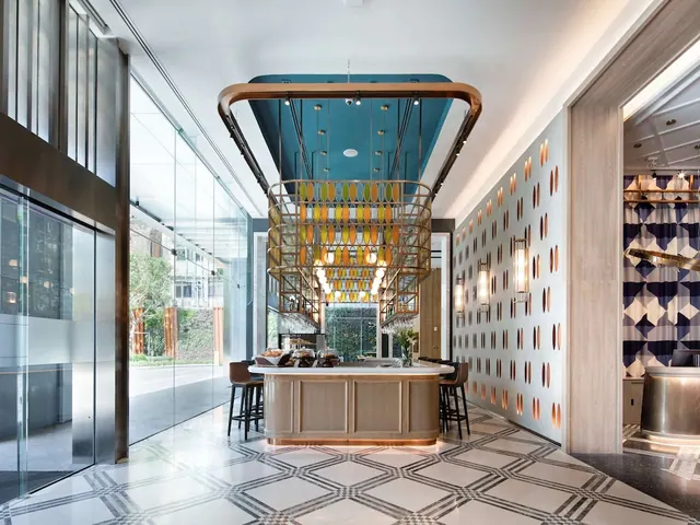 A lobby with a central counter holding pastries under a large colourful pendant light, with floor-to-ceiling glass walls looking out onto trees and greenery.