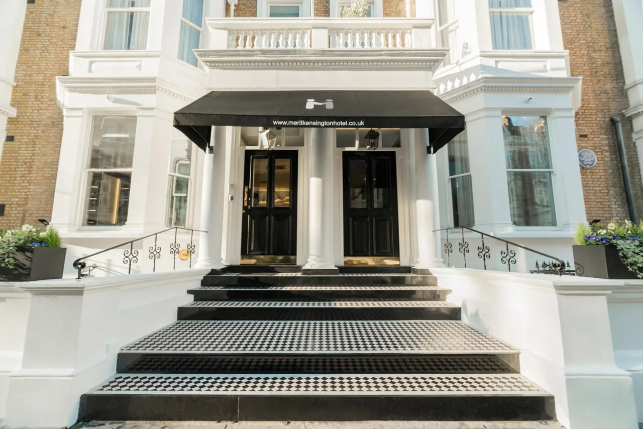 The white facade of a hotel entrance with a black awning, a flight of steps with a checkered tread, and black double doors.