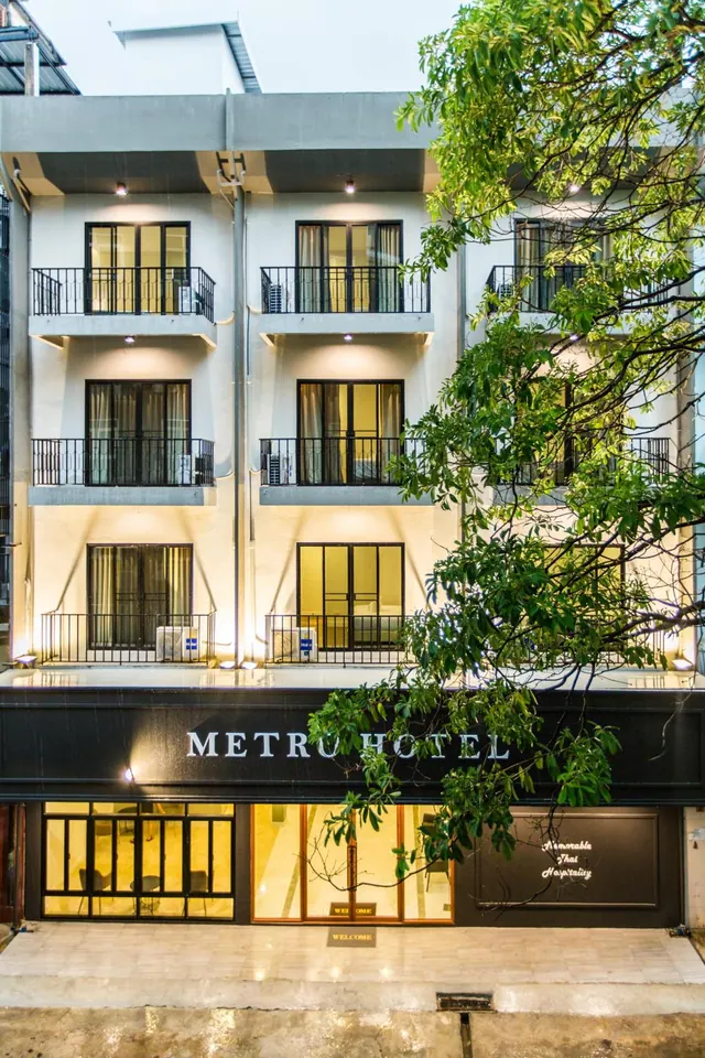 Exterior of the Metro Hotel building at dusk, with lit balconies, air conditioning units, and a tree in the foreground.