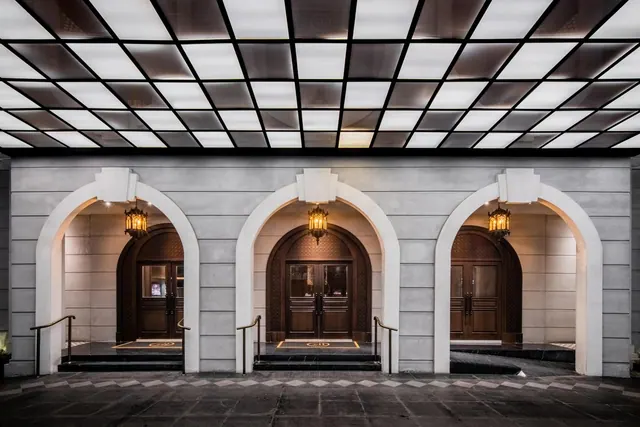 The front facade of a building with three arched entrances, hanging lanterns, and an illuminated grid ceiling over the entrance canopy.