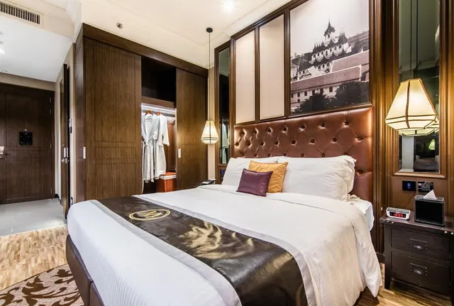 A bedroom with a made king bed, a tufted leather headboard, a framed black-and-white photo of a historic building, and an open wardrobe holding bathrobes.