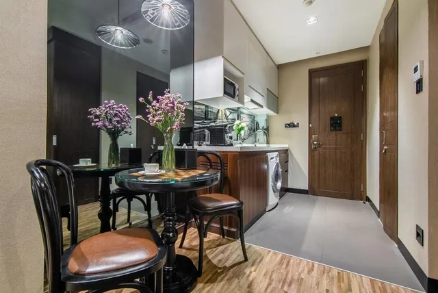 A small room with two round dining tables and black bistro chairs, a kitchenette with a microwave and sink, and a wooden entrance door.