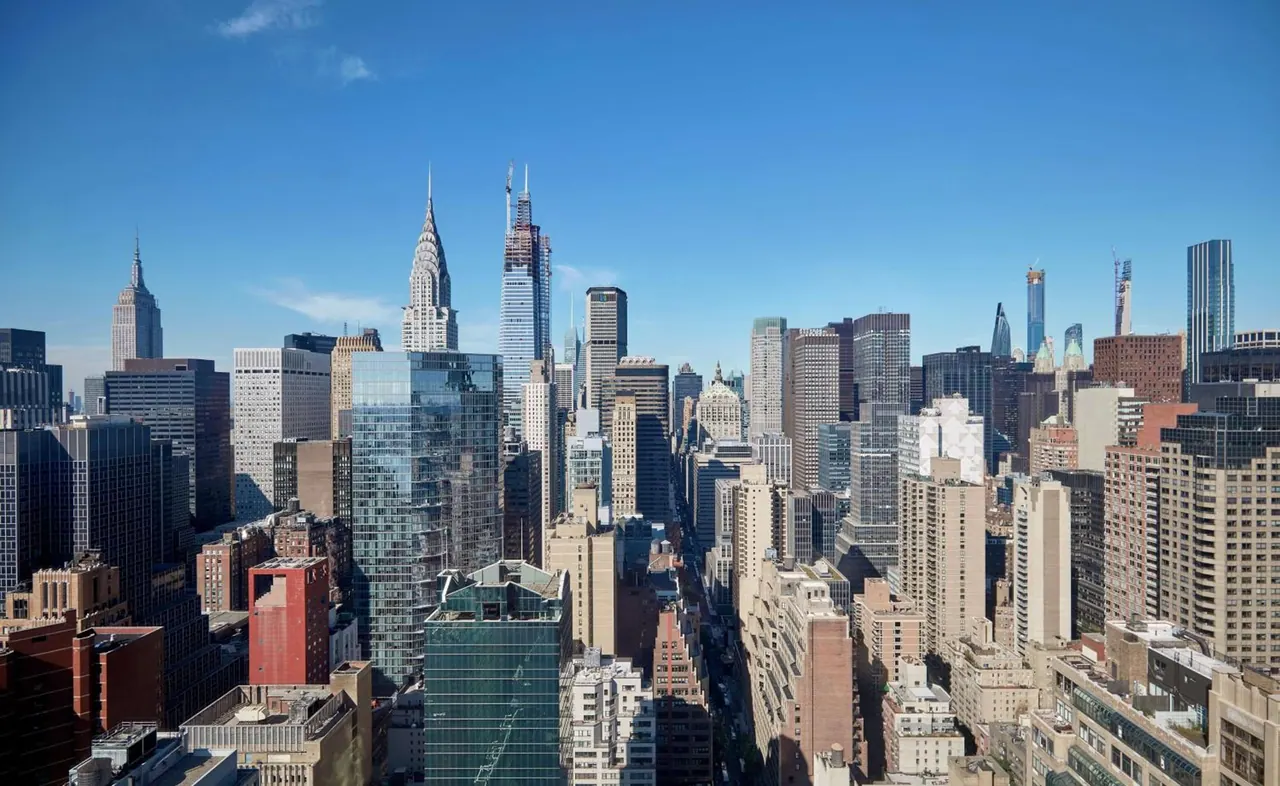 Elevated view over a dense Manhattan skyline with the Empire State Building and Chrysler Building visible under a clear blue sky.