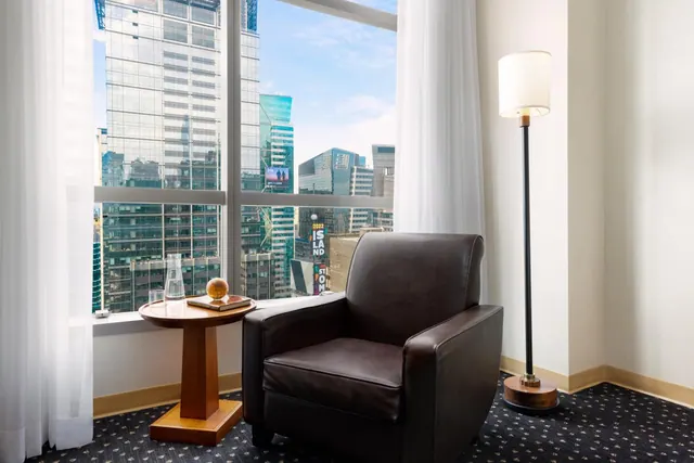 A leather armchair, side table and floor lamp sit in a corner beside a window overlooking city skyscrapers.