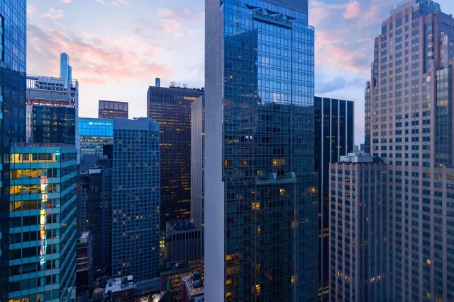 A view across tall glass and stone office towers at dusk, with a Barclays sign visible on one building.
