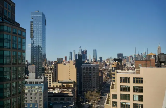 A view over a dense city of mid-rise buildings and skyscrapers under a clear blue sky, with the Empire State Building visible on the right.