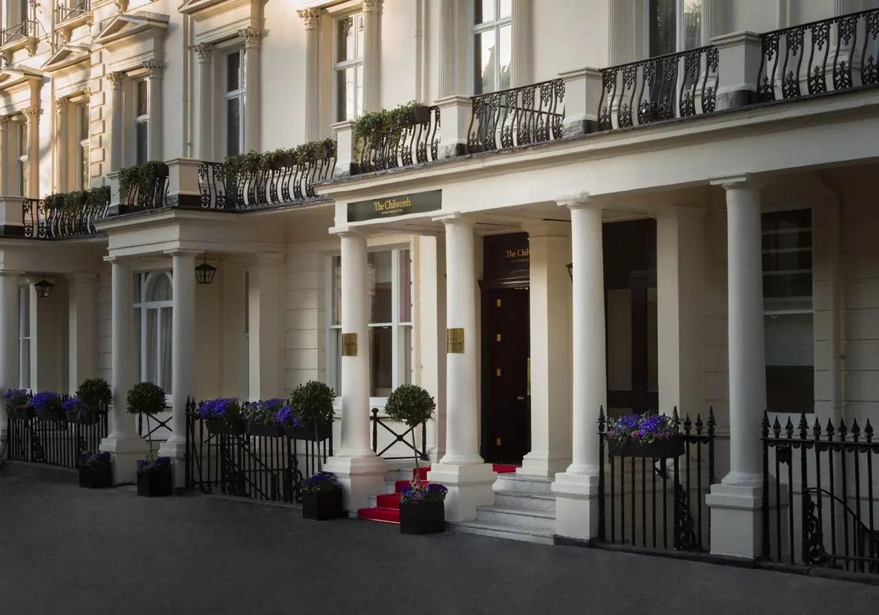 Exterior of a cream-coloured Georgian-style townhouse hotel with white columns, black iron balconies, and a red-carpeted entrance beneath a sign reading The Chilworth.