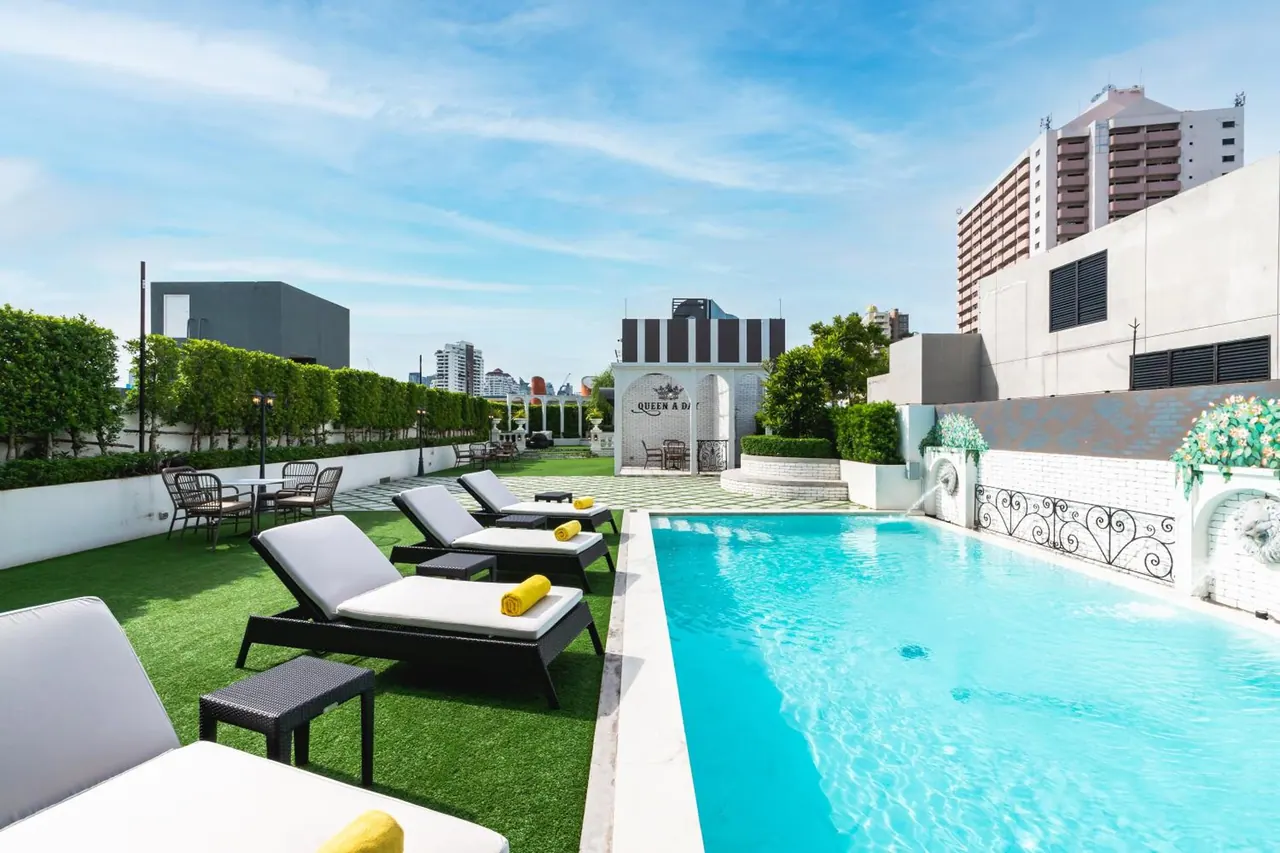 A rooftop swimming pool with sun loungers on artificial turf, a white pavilion and high-rise buildings in the background.