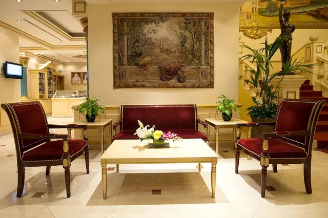 A lobby seating area with red velvet armchairs and a sofa, a coffee table with flowers, and a large tapestry on the wall.