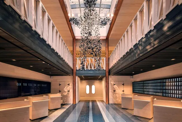 A lobby with a suspended black sculpture hanging from a skylit atrium, light wood benches on the floor, and text panels along the walls.