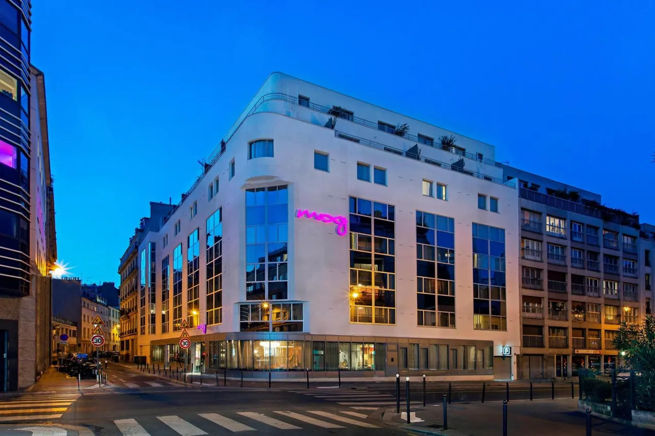 A modern white hotel building stands at a Paris street intersection at dusk.