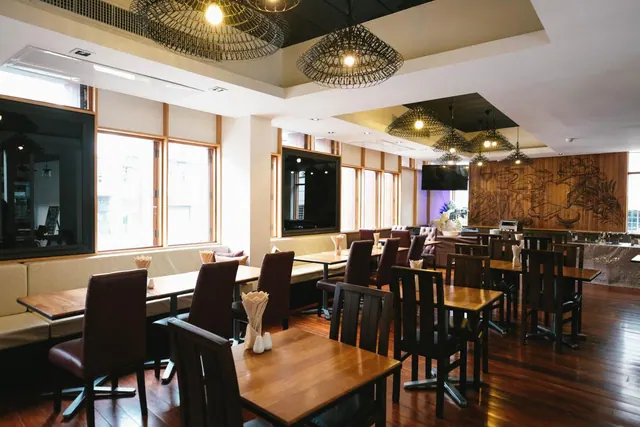 A restaurant dining room with wooden tables, leather chairs, woven pendant lights, banquette seating and a carved wooden wall.
