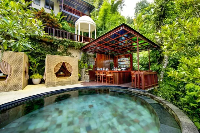 A small round pool in the foreground sits beside an open-sided wooden bar pavilion with stools, lattice cabanas and a white gazebo, all surrounded by jungle greenery.