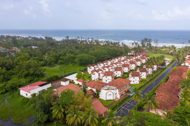 An aerial view shows a tropical resort surrounded by palm trees with the sea beyond.