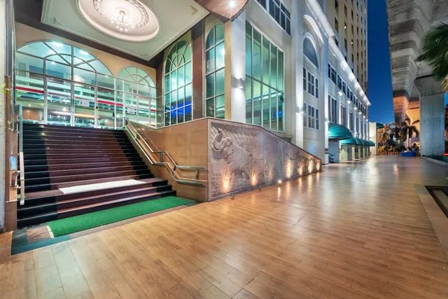 Illuminated entrance of a building at night, with a staircase, a green carpet at its base, and an elephant relief on the wall beside it.