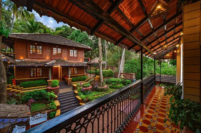 A covered veranda overlooks a landscaped courtyard and traditional tiled-roof building surrounded by tropical greenery.