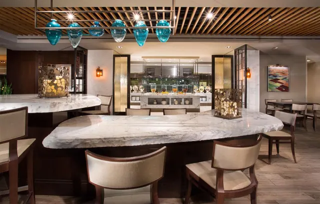 A dining area with a marble-topped counter, upholstered chairs, blue glass pendant lights and a buffet counter in the background.