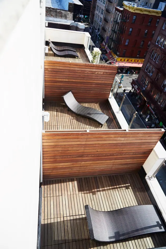 Two wooden-decked terraces with lounge chairs overlook a street lined with brick buildings and signage.