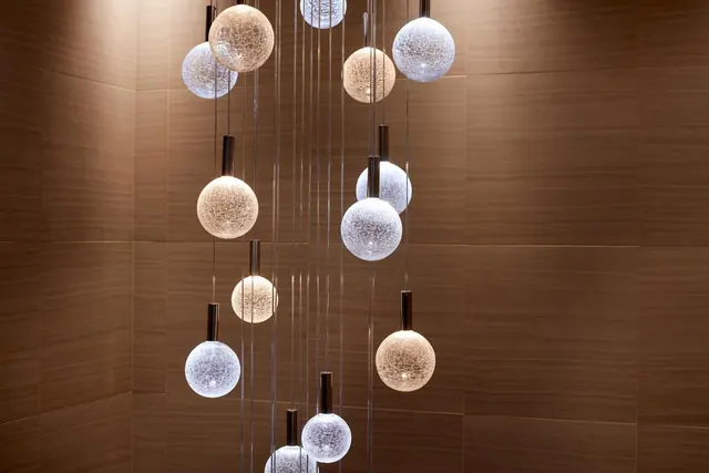 A cluster of crackled-glass globe pendant lights hangs at varying heights in front of a wood-panelled wall.