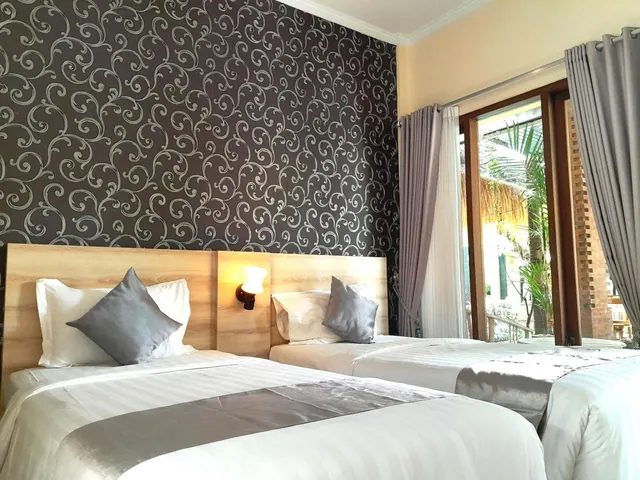 A bedroom with two beds with grey pillows against a patterned dark wall, with a window looking out onto palm trees.