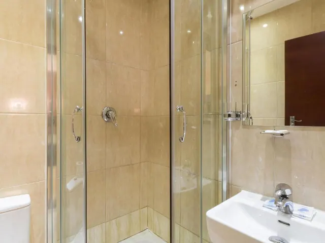 A bathroom with a glass-enclosed walk-in shower, beige tiled walls, a wall-mounted shower valve, a white basin with a chrome tap, and a mirror.