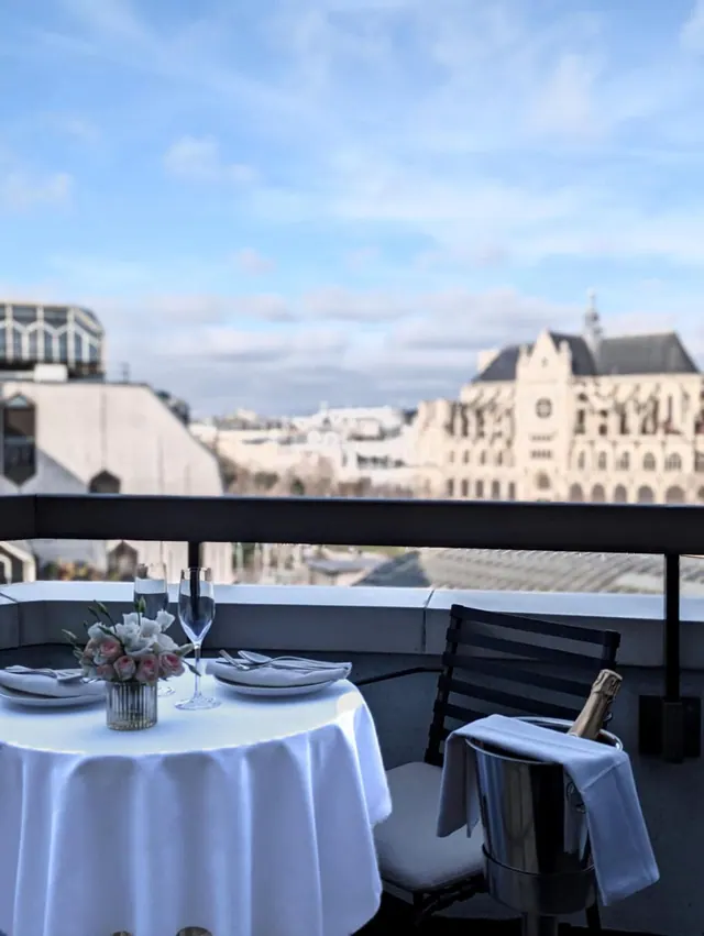 A set dining table with flowers and champagne overlooks the city from an outdoor terrace.