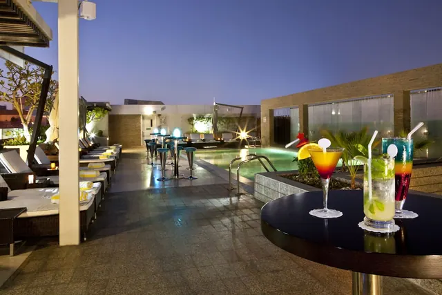 A rooftop pool at dusk with sun loungers, bar stools and cocktails on a high table in the foreground.