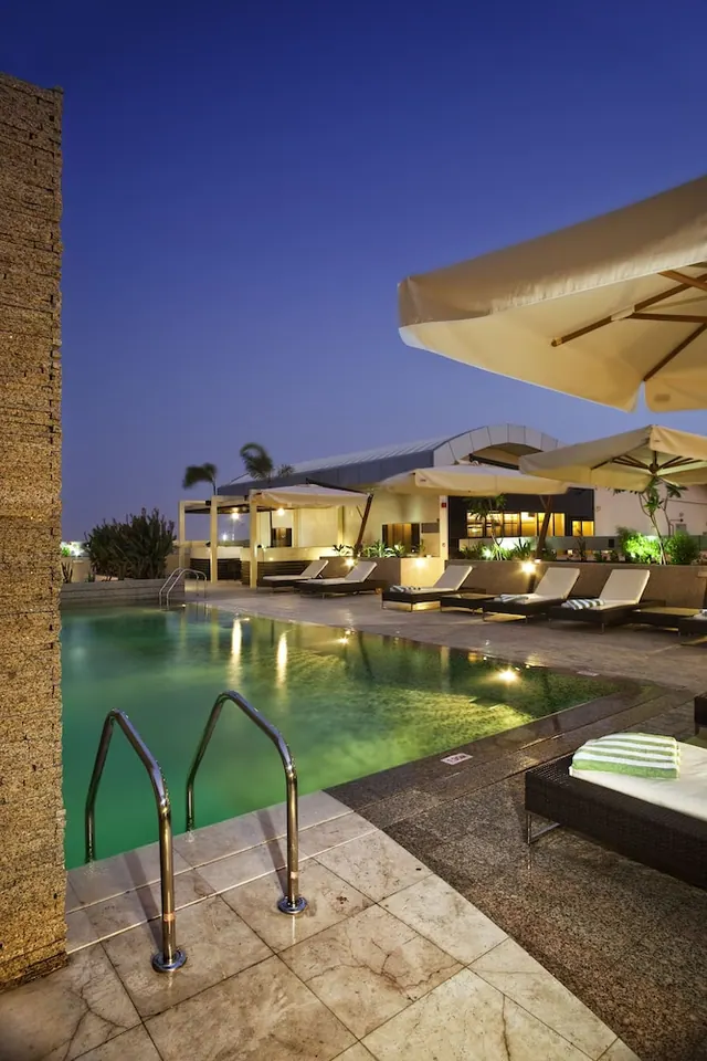 Illuminated swimming pool at dusk with sun loungers, cabanas and parasol umbrellas along the deck.