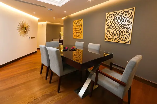 A dining area with a dark glossy table, grey upholstered chairs, wood flooring and gold decorative panels on the wall.