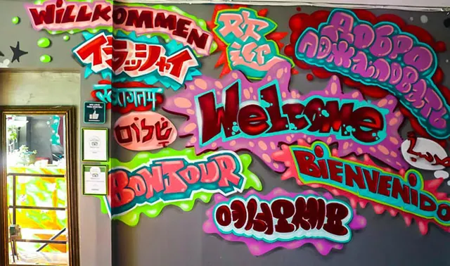 A colourful graffiti-style wall displays the word welcome in several languages beside a doorway with framed certificates.