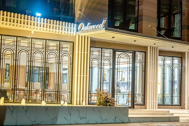 Night view of the Oakwood building exterior with ornate metal window screens, glass entrance doors, a marble planter wall and steps.