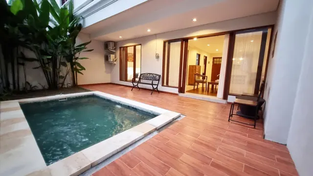 A small private plunge pool sits on a tiled terrace beside a glass-doored room, with tropical plants at the left and wall air conditioners above.