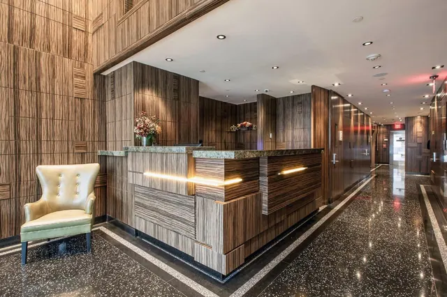 A lobby reception desk with wood-panelled walls, an armchair, and a terrazzo floor leading down a corridor.
