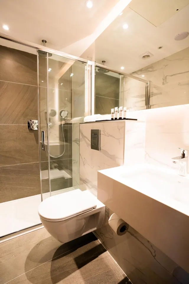 A bathroom with a walk-in shower behind a glass sliding door, a wall-hung toilet, a wall-mounted basin and a large mirror.